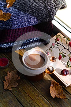 Large Cup of cappuccino on vintage brown background. Autumn, fall leaves, hot steaming cup of coffee and a warm scarf on wooden ta