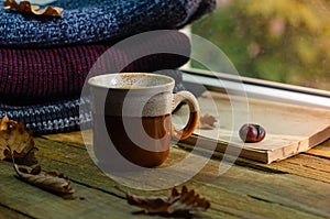Large Cup of cappuccino on vintage brown background. Autumn, fall leaves, hot steaming cup of coffee and a warm scarf on wooden ta