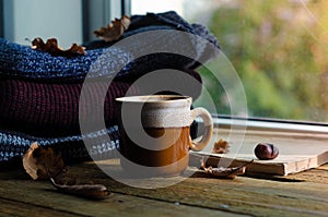 Large Cup of cappuccino on vintage brown background. Autumn, fall leaves, hot steaming cup of coffee and a warm scarf on wooden ta