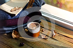 Large Cup of cappuccino on vintage brown background. Autumn, fall leaves, hot steaming cup of coffee and a warm scarf on wooden ta