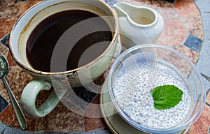 A large Cup of coffee, Chia pudding on coconut milk with a mint leaf and cream in a milk jug on the table