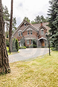 Large detached house exterior with brick walls and red roof behind a cobblestone path and green lawn in the summer