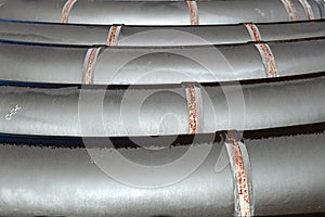 Large diameter black gasification pipes lie in a row in an open warehouse on the street on a summer day.