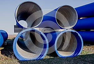 Large diameter blue concrete pipes lie in the field