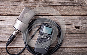 Large diaphragm condenser studio microphone and recorder on wooden background.