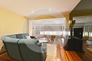 Large dining room with white wood and glass window, green fabric sofa and reddish wood floors