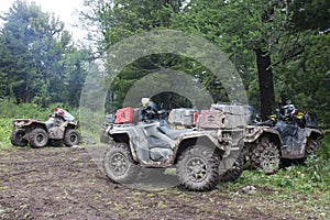 Large dirt-covered ATVs with red cans standing in a coniferous forest