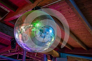 Large disco mirror ball reflecting colorful lights hanging from a wooden ceiling