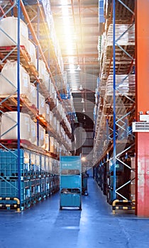 Large distribution warehouse interior, pallets and boxes of cargo stack on row of high shelves.