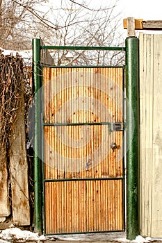 A large door a gate in the fence is made of a metal frame and wooden bars