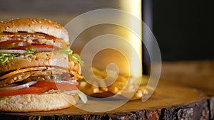 A large double burger with chicken is laying on a wooden board next to french fries. Professionally cooked fast food.