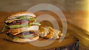 A large double burger is lying on a wooden board next to french fries. Professionally cooked fast food.