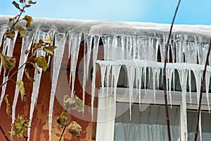 Large double icicles hanging from the roof and above a plastic window against the blue sky