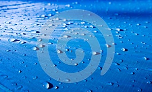 Large drops of water on a blue textile with a waterproof effect. Water-repellent impregnation.