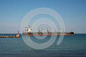 A large dry cargo ship leaves the port past the breakwater.