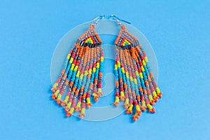 Large earrings made of multi-colored beads and bugle beads, boho style, on a blue background
