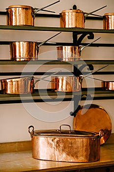 Large elongated pan on the countertop with ladles and saucepans made of copper on the shelves, in different sizes on