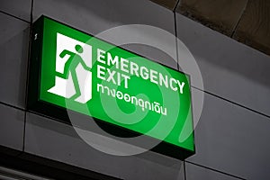 Large Emergency exit sign green light box is placed on the wall of exhibition hall. Thai Letter is Thai Language on the green