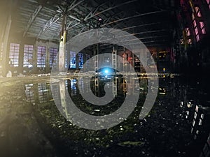 Large empty abandoned warehouse building or factory workshop at night with reflection in water, abstract ruins background