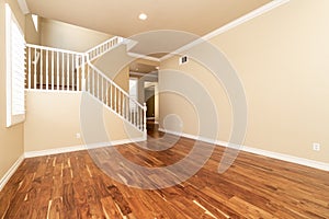 Large empty room with wood floor, molding and windows and stairs.