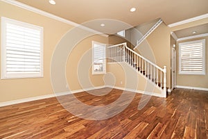 Large empty room with wood floor, molding and windows and stairs.