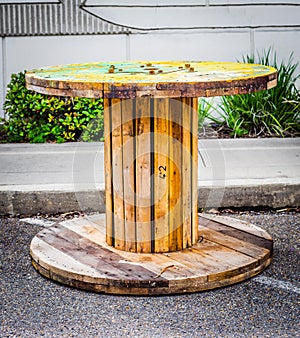 Large Empty Wooden Spool on asphalt, and a white stripped pattern wall in the background.