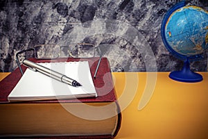 A large encyclopedia book and a notebook with a pen lie on the desk