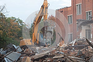 A large excavator breaks down the house, demolishing a building in the city