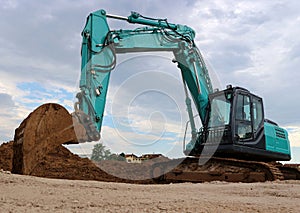 Large excavator with the scoop in the dirt, against a gray cloudy sky