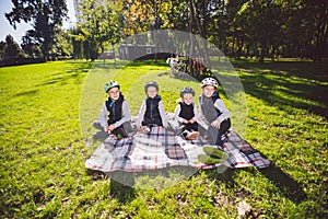 Large family Caucasian children. Three brothers and sister sitting resting on blanket outside the park. Green lawn grass