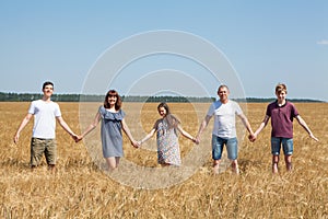 Large family from father, mother, two brothers and sister holding hands in line on a wheat field, full length portrait