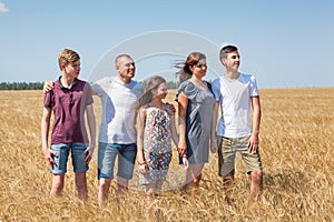 Large family from father, mother, two brothers and sister standing in line on wheat field, full length portrait