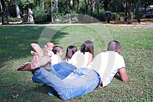 Large family of five lying on the grass in a park, seen from the back and feet up. Father, mother and three children. Family