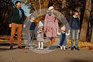 Large family with four kids holding hands and stand on road at autumn park