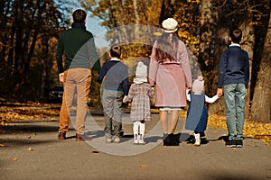 Large family with four kids holding hands and stand on road at autumn park, back view