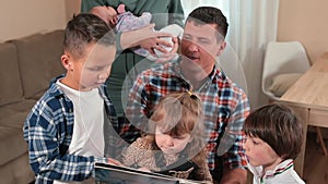 Large family reads book home father holds daughter in arms, next to his sons.