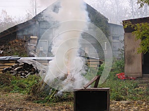 A large fire with smoke burning dry grass in the yard near a wooden house in the fall