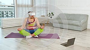 Large fitness man with virtual glasses doing yoga exercises. Plus size body positive practice yoga with laptop at home