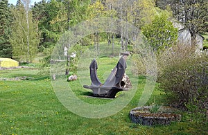 Large five tons ship anchor is mounted on green grass on a sunny spring day