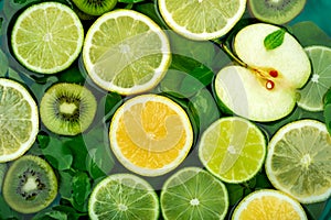 Large flat round slices of different fruits and citrus such as lime and lemon float together with kiwi, apple, orange and green