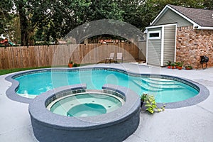 A large free form gray grey accent swimming pool with turquoise blue water in a fenced in backyard in a suburb