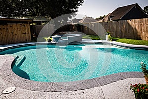 A large free form gray grey accent swimming pool with turquoise blue water in a fenced in backyard in a suburb