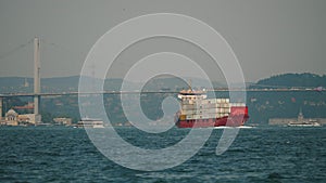Large freight ship full of containers sailing under Bosphorus Bridge
