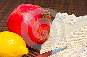 Large fresh fruit of pomegranate and lemon with a woven napkin and a knife on a bamboo mat, still life, close-up