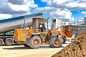 A large front loader transports crushed stone or gravel in a bucket at a construction site or concrete plant. Transportation of