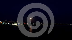 Large full moon moves across sky glowing and reflecting on the ocean. Captured in Estoril, Portugal