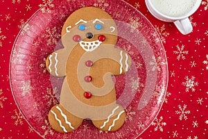 Large gingerbread cookie on a glass platter, red fabric background with gold snowflakes, white mug with milk