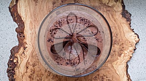 Large glass bowl of chocolate mousse standing on an olive wood platter, decorated with chocolate shavings and curls.