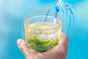 Large glass of cocktail with mint and lemon in hand on a blue background close-up