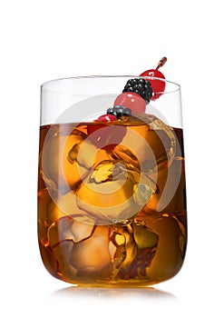 Large glass with ice cubes of old fashioned whiskey cocktail with cherry and blackberry on white background